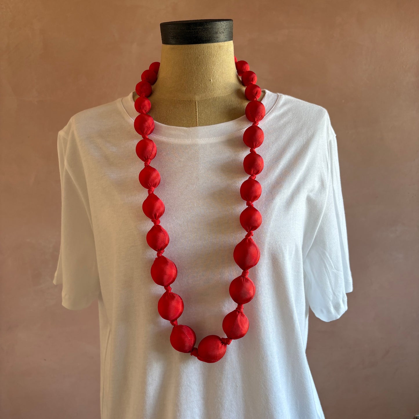 A red beaded necklace draped over a white shirt on a dress form mannequin against a plain brown background.
