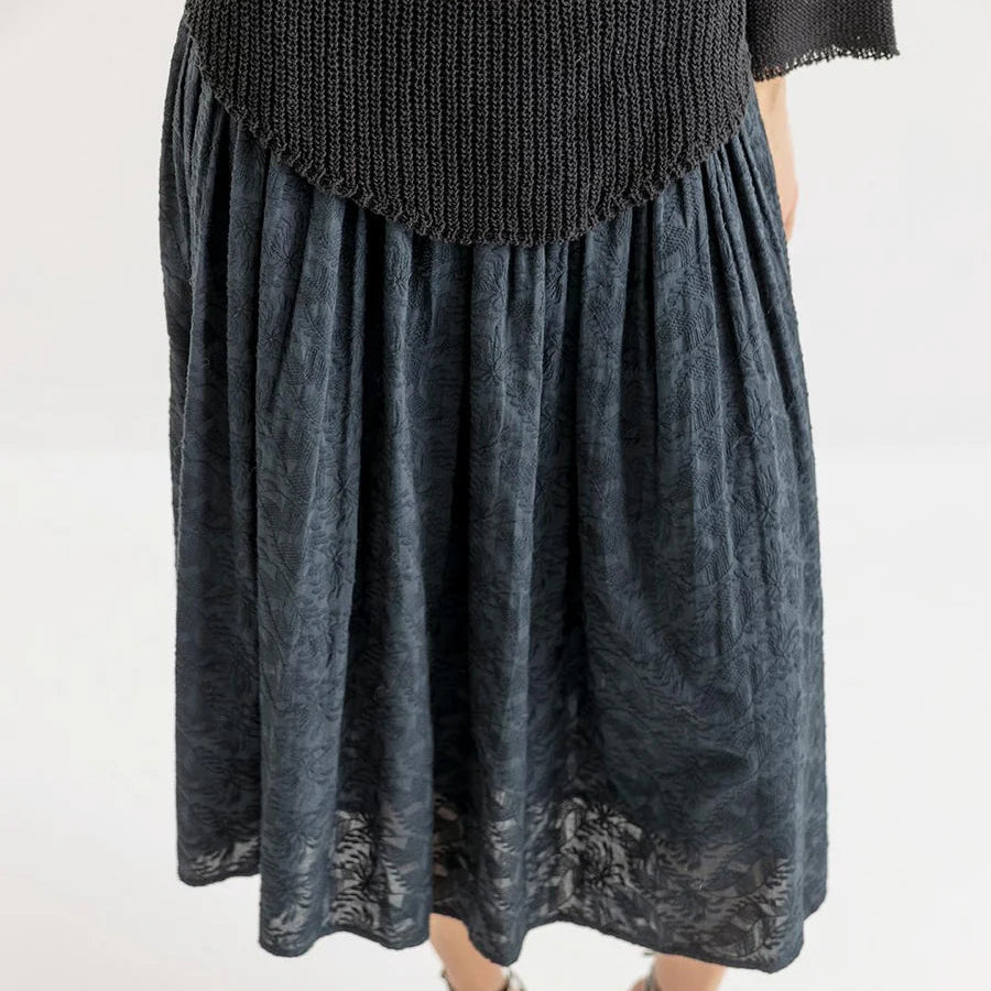 Person wearing a black knit sweater and dark denim skirt on a white background
