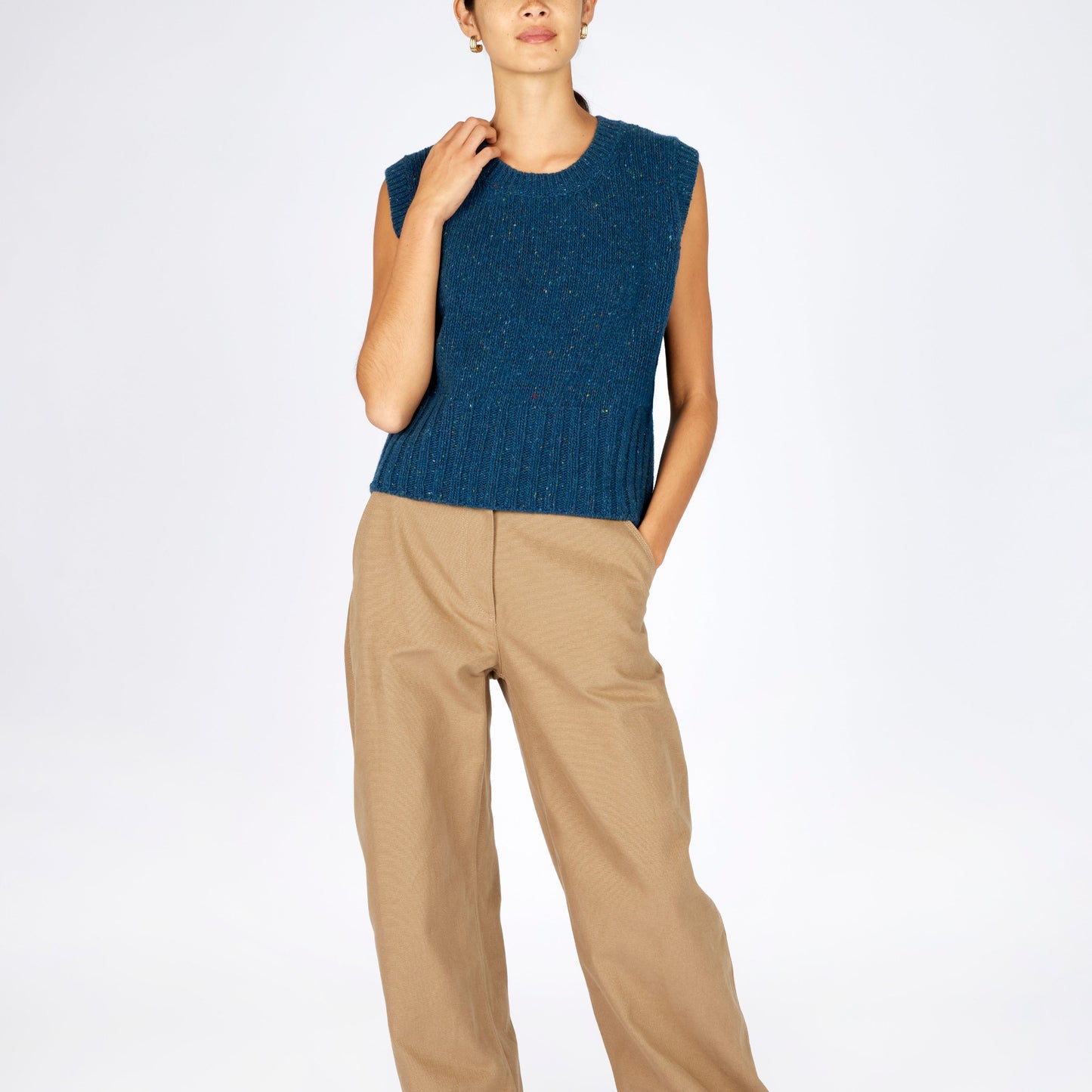 Person wearing a blue sleeveless top and beige pants on a white background