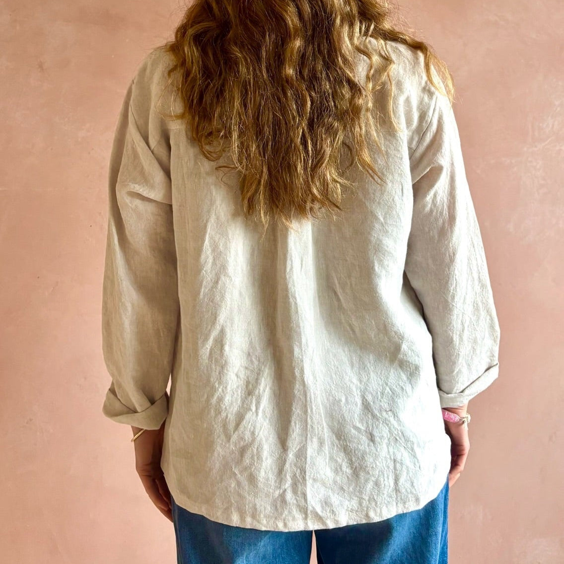 Person wearing a light-colored shirt against a pink wall