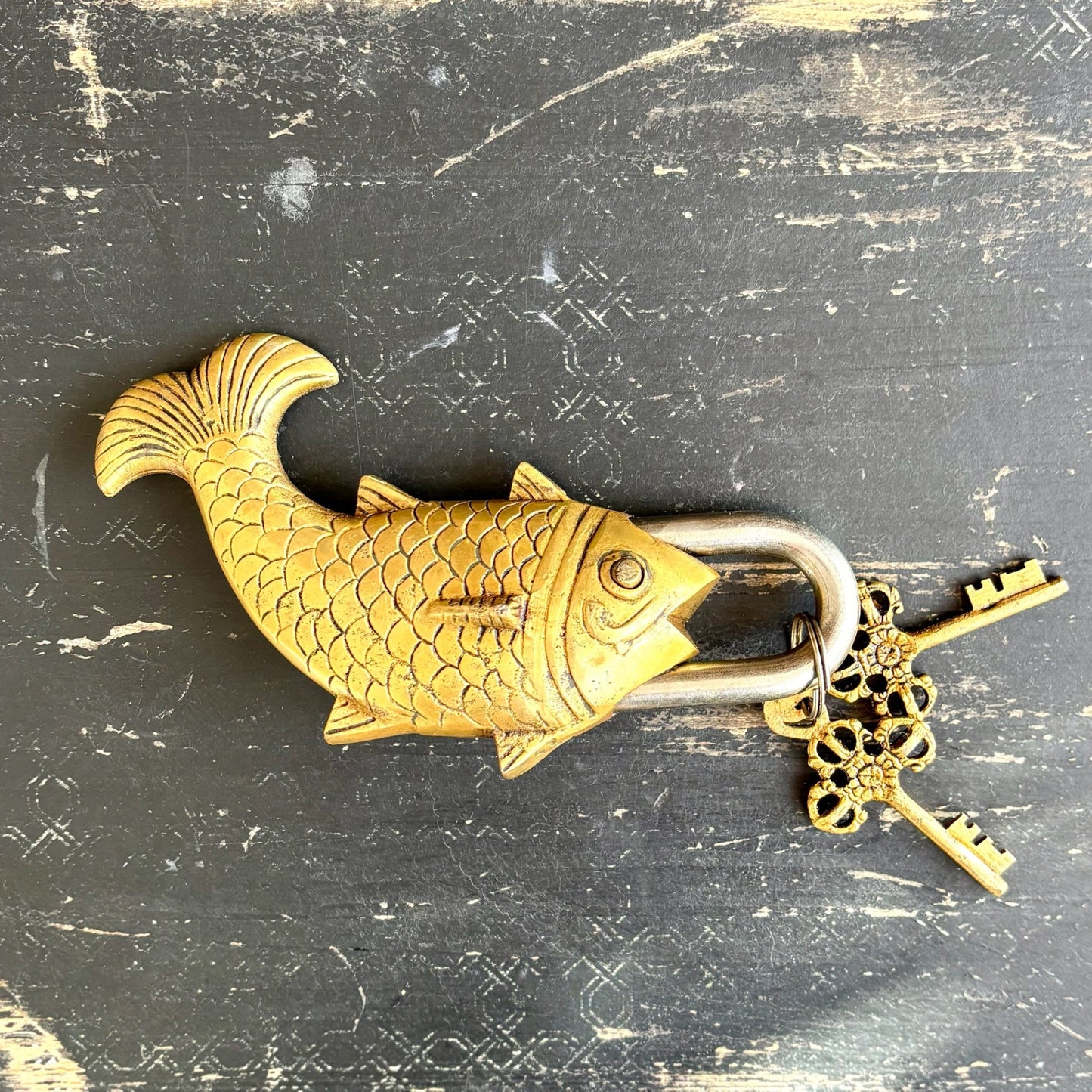 Gold fish-shaped padlock with a key on a textured black background