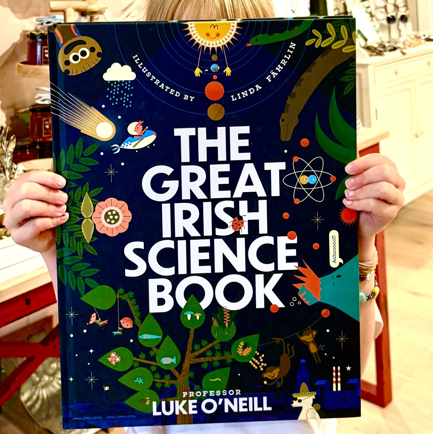 Person holding 'The Great Irish Science Book' with colorful illustrations on a dark blue background.
