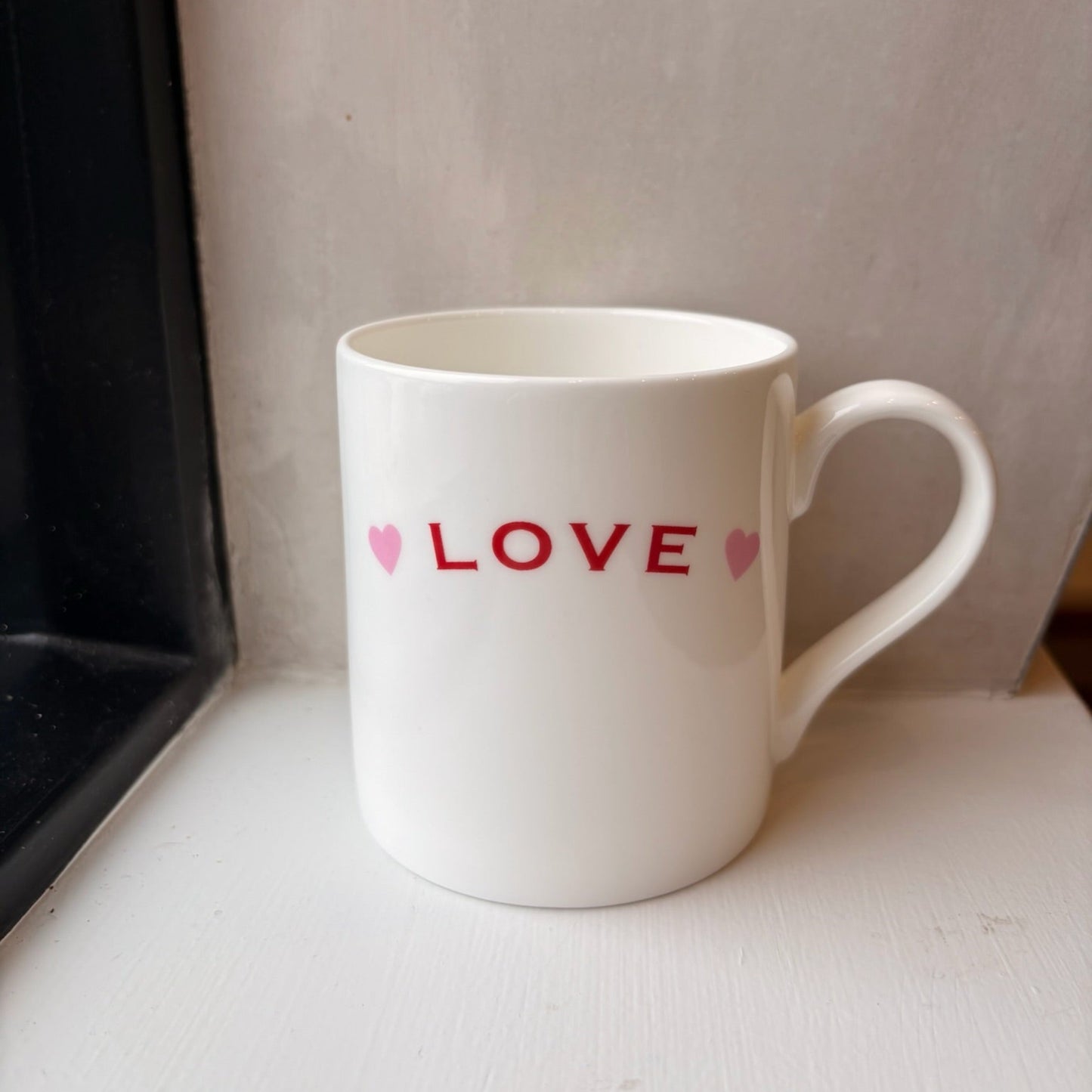 White mug with 'LOVE' and heart designs on a light surface.