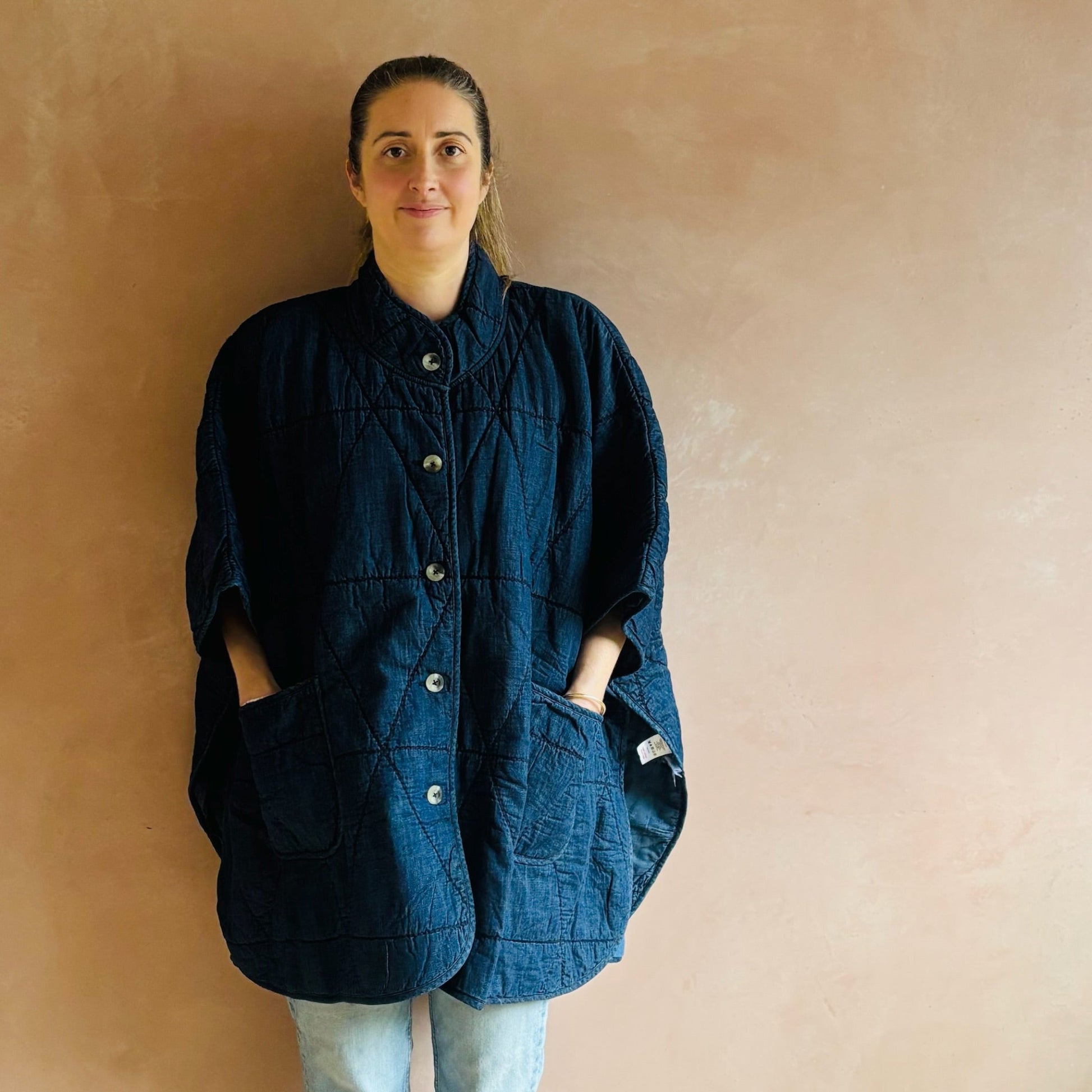 Person wearing a blue jacket against a beige wall