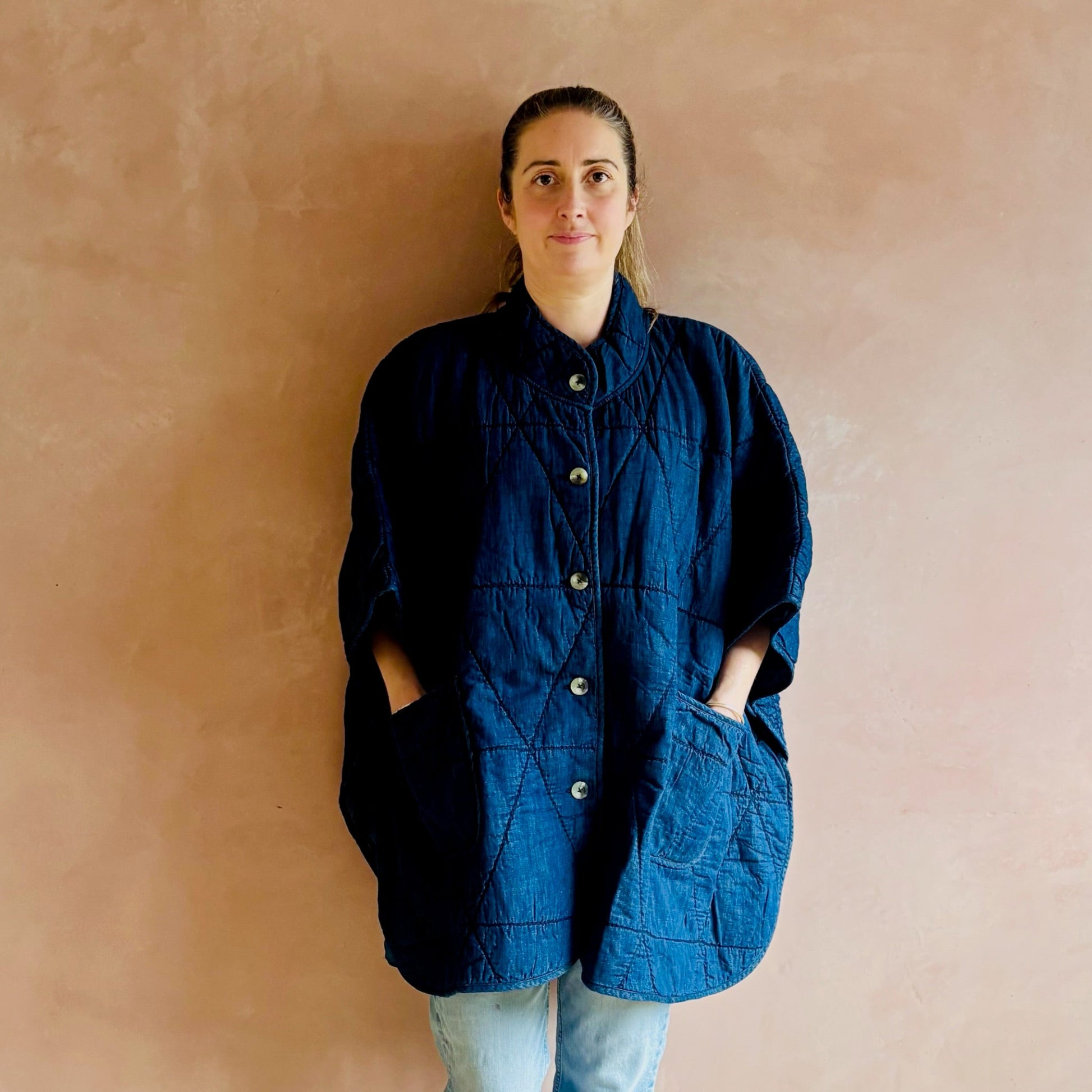 Woman wearing a blue jacket against a beige wall