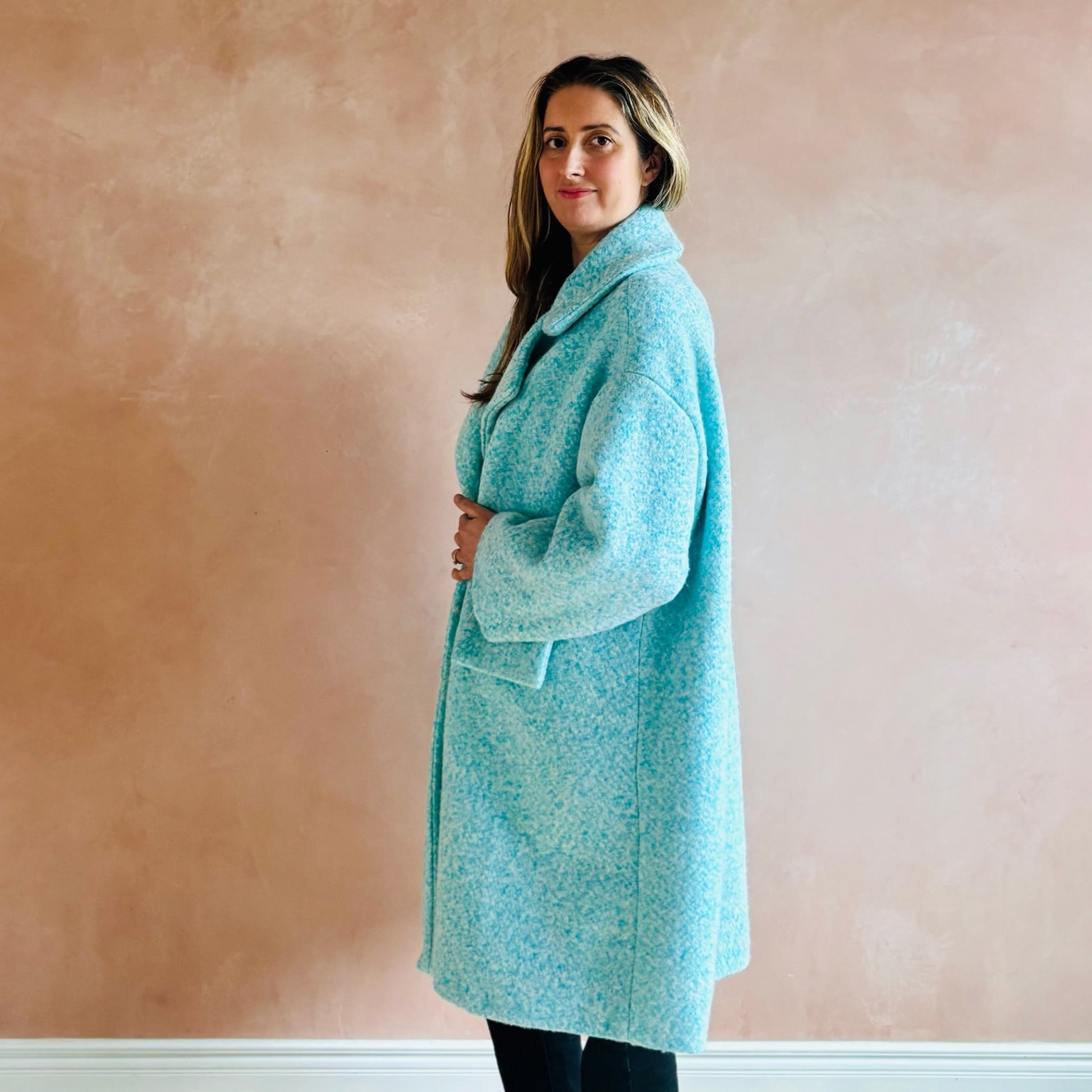 Woman wearing a light blue coat against a pink wall