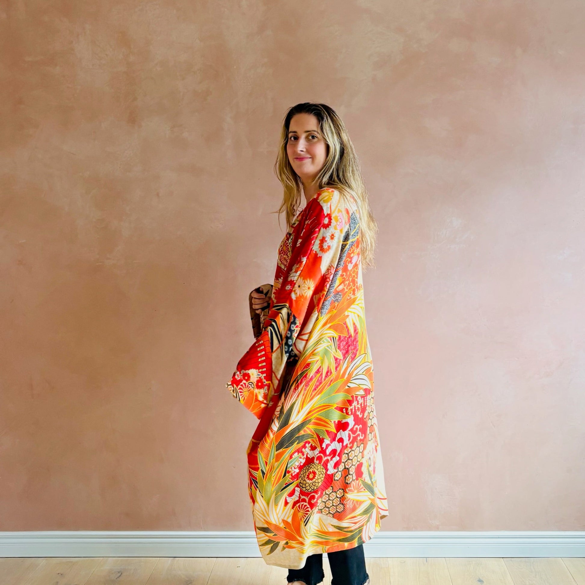 Woman wearing a colorful floral dress against a plain wall.