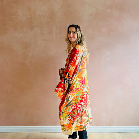 Woman wearing a colorful floral dress against a plain wall.
