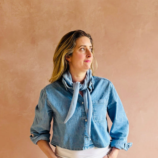 Woman wearing a denim jacket and scarf against a beige background