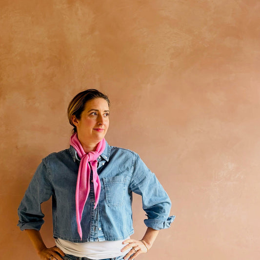 Woman wearing a denim shirt and pink scarf against a beige wall