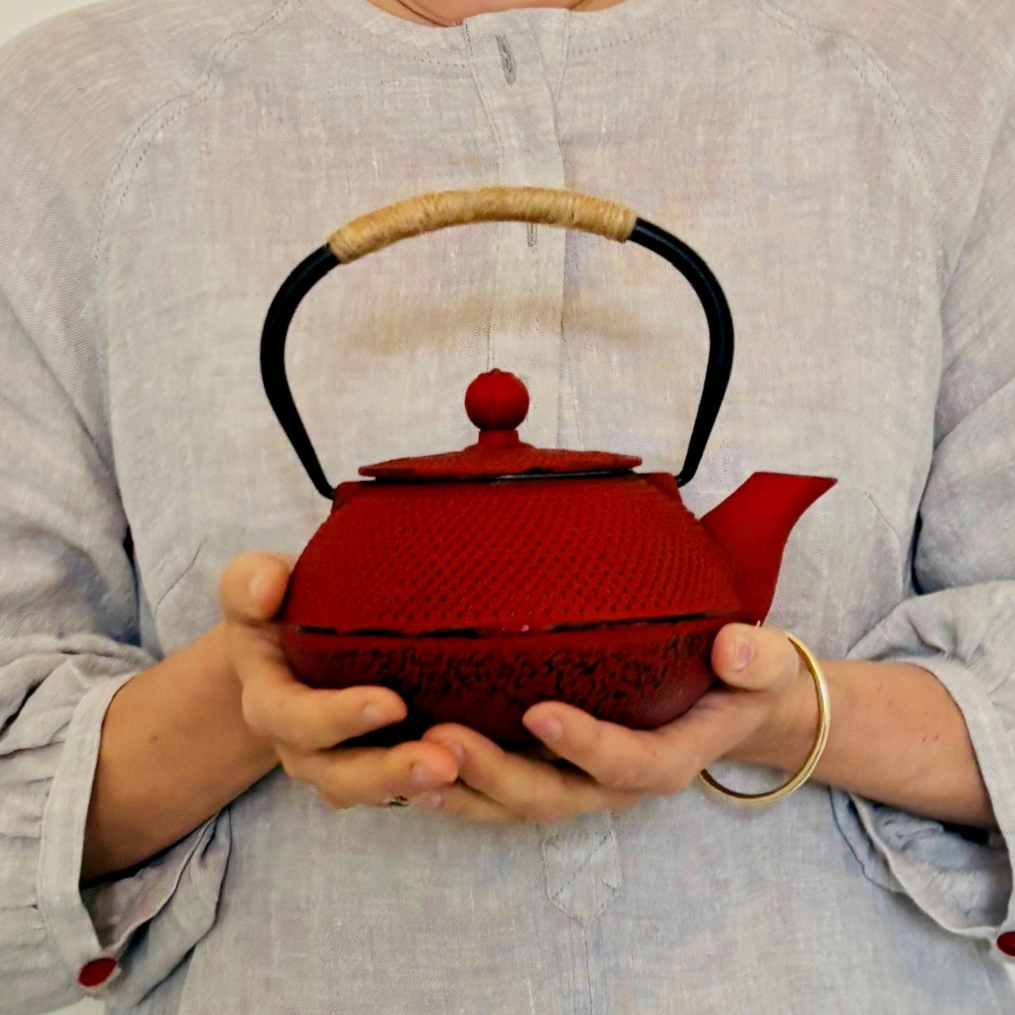Red teapot held by a person wearing a light gray shirt