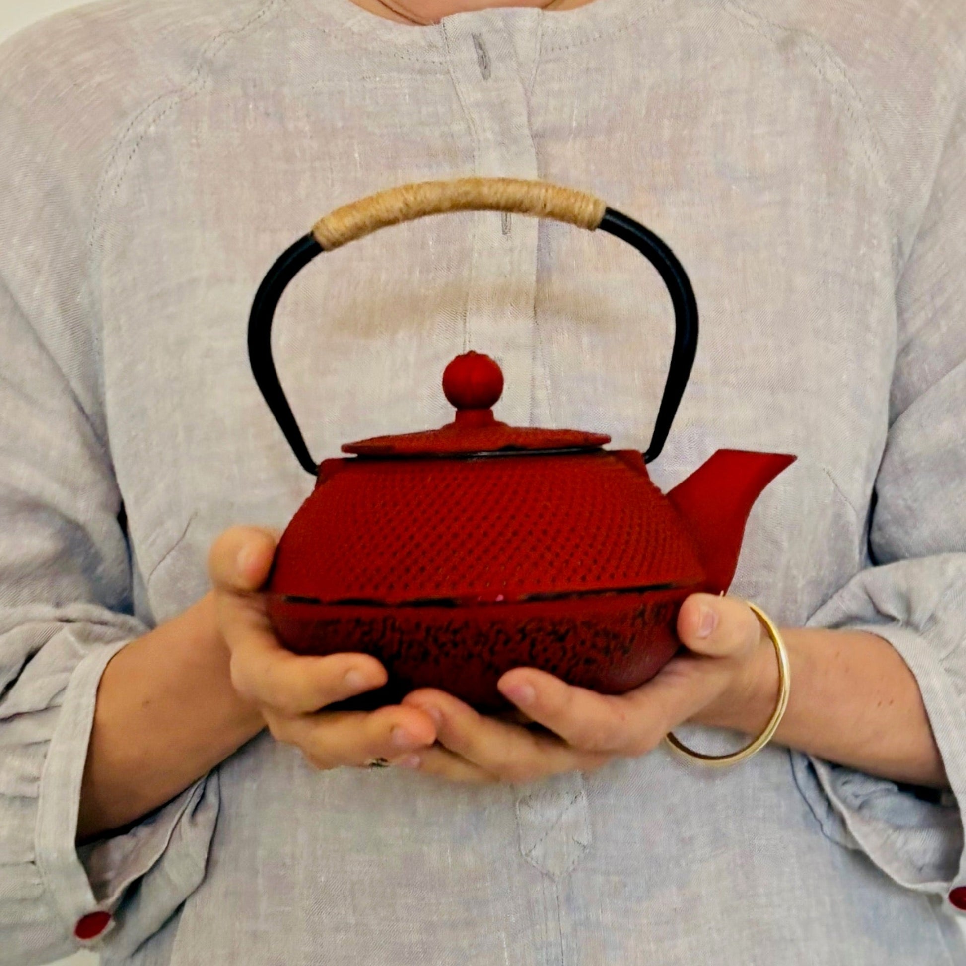Red teapot held by a person wearing a light gray shirt