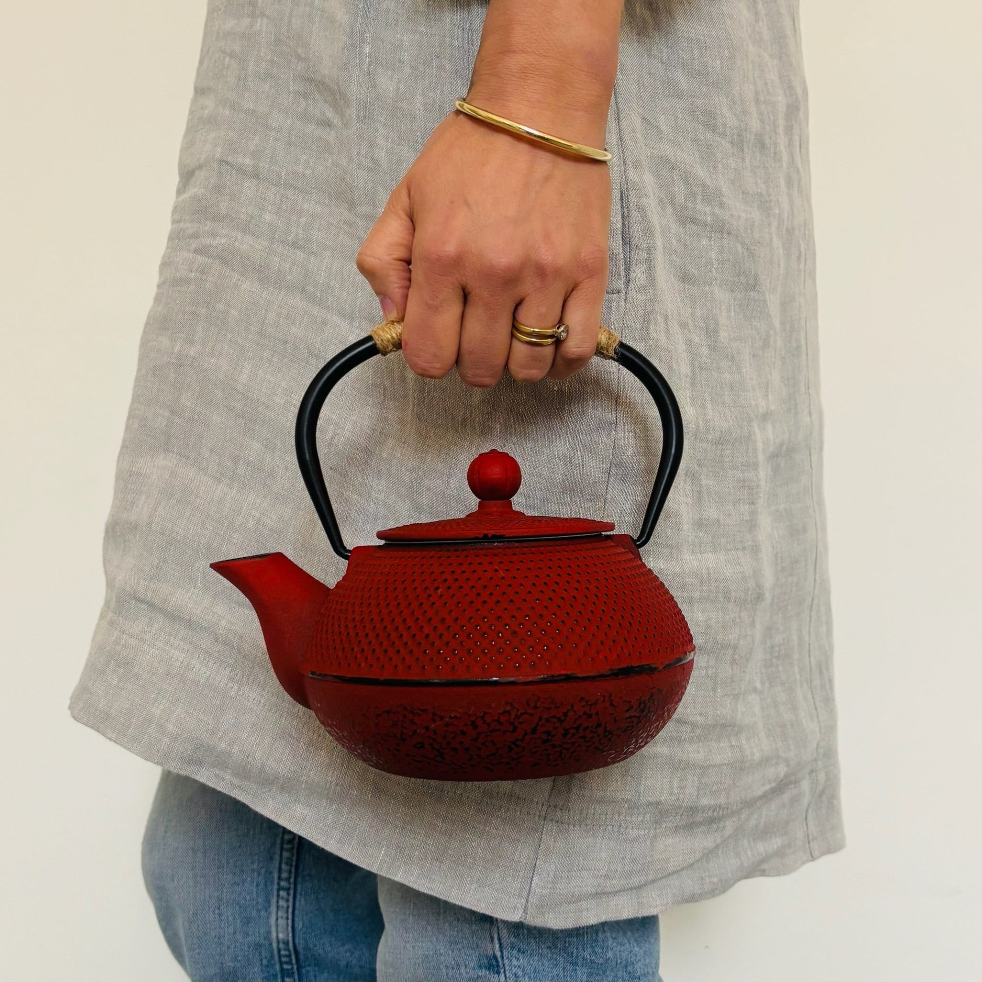 Person holding a red teapot with a black handle against a neutral background