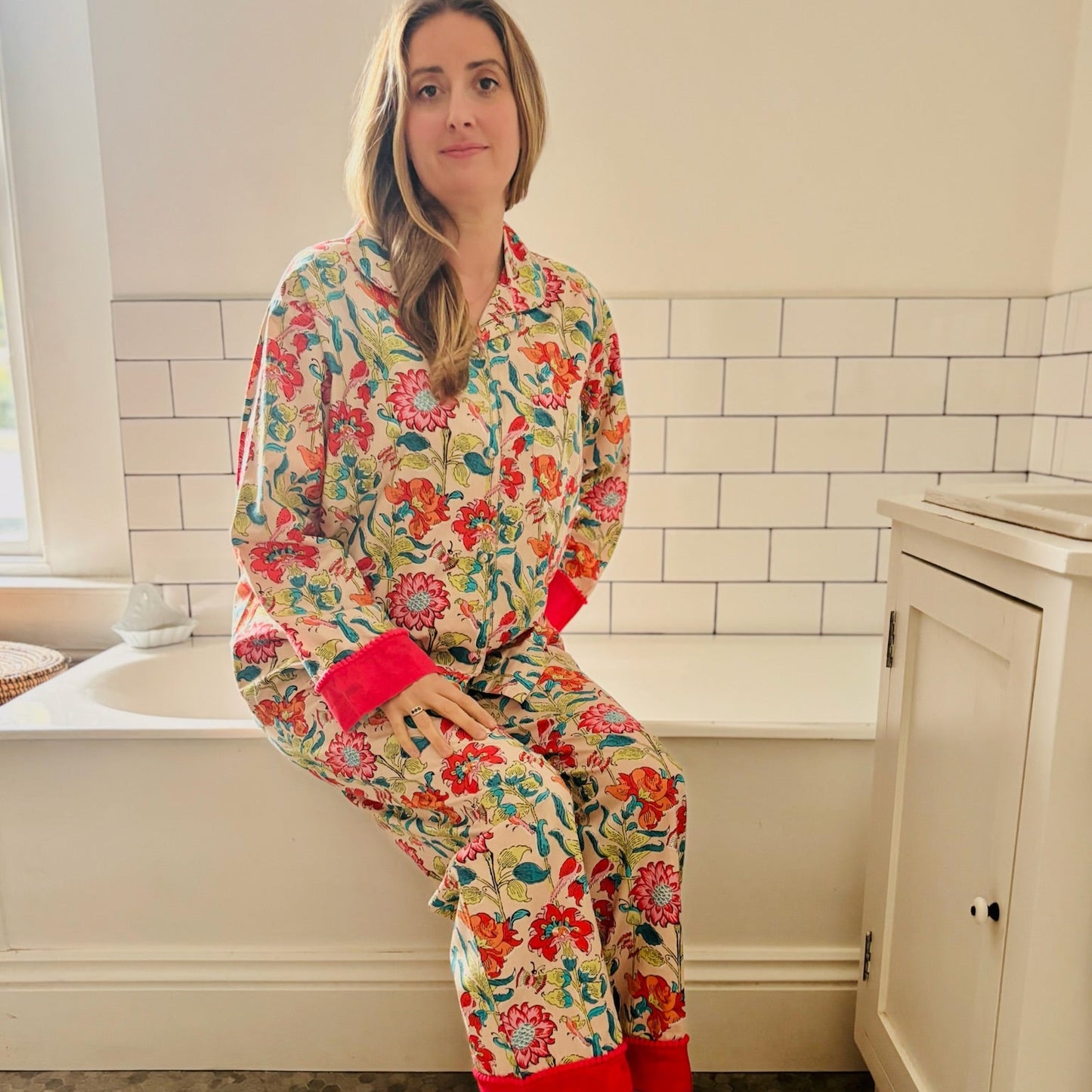 Woman wearing colorful floral pajamas sitting on a bathtub edge in a bathroom.