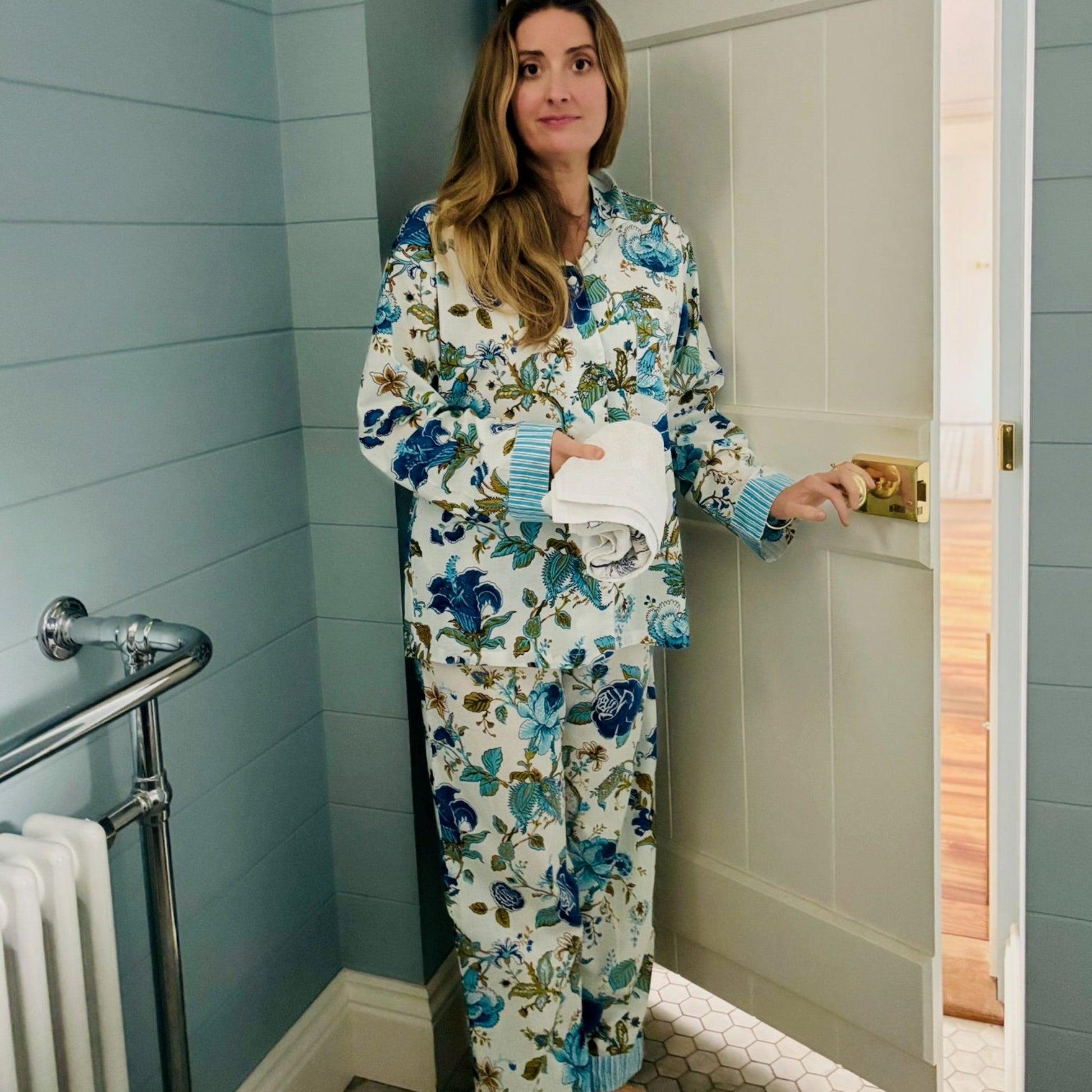Woman in floral pajamas standing in a bathroom.