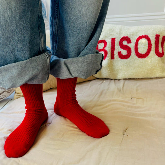 Person wearing red socks with blue jeans on a beige surface, with 'BISOU' text in the background.