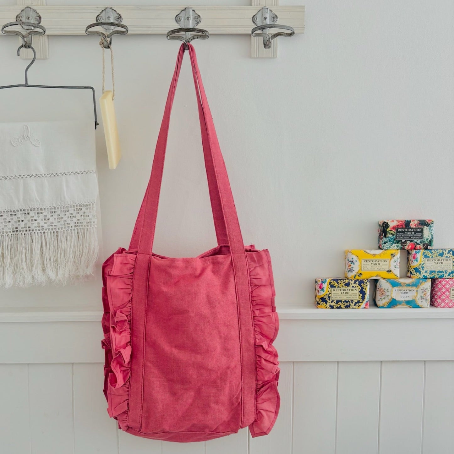 Pink tote bag hanging on a hook with stationery items on a shelf in the background.