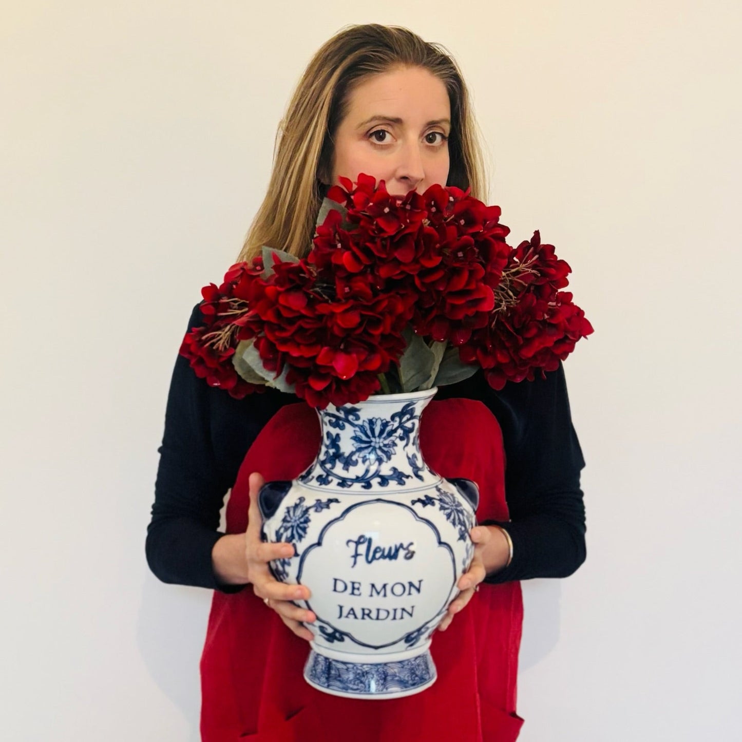 Person holding a large bouquet of red flowers and a decorative vase with a white background