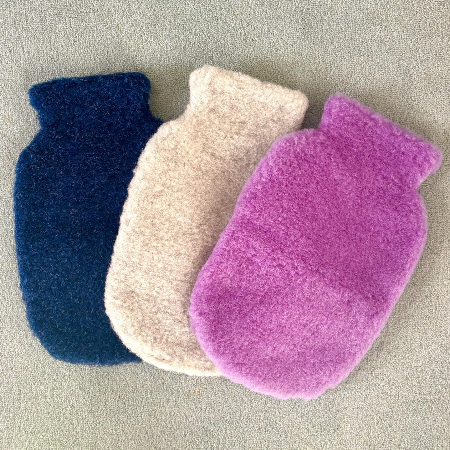 Three colorful hot water bottles on a neutral background