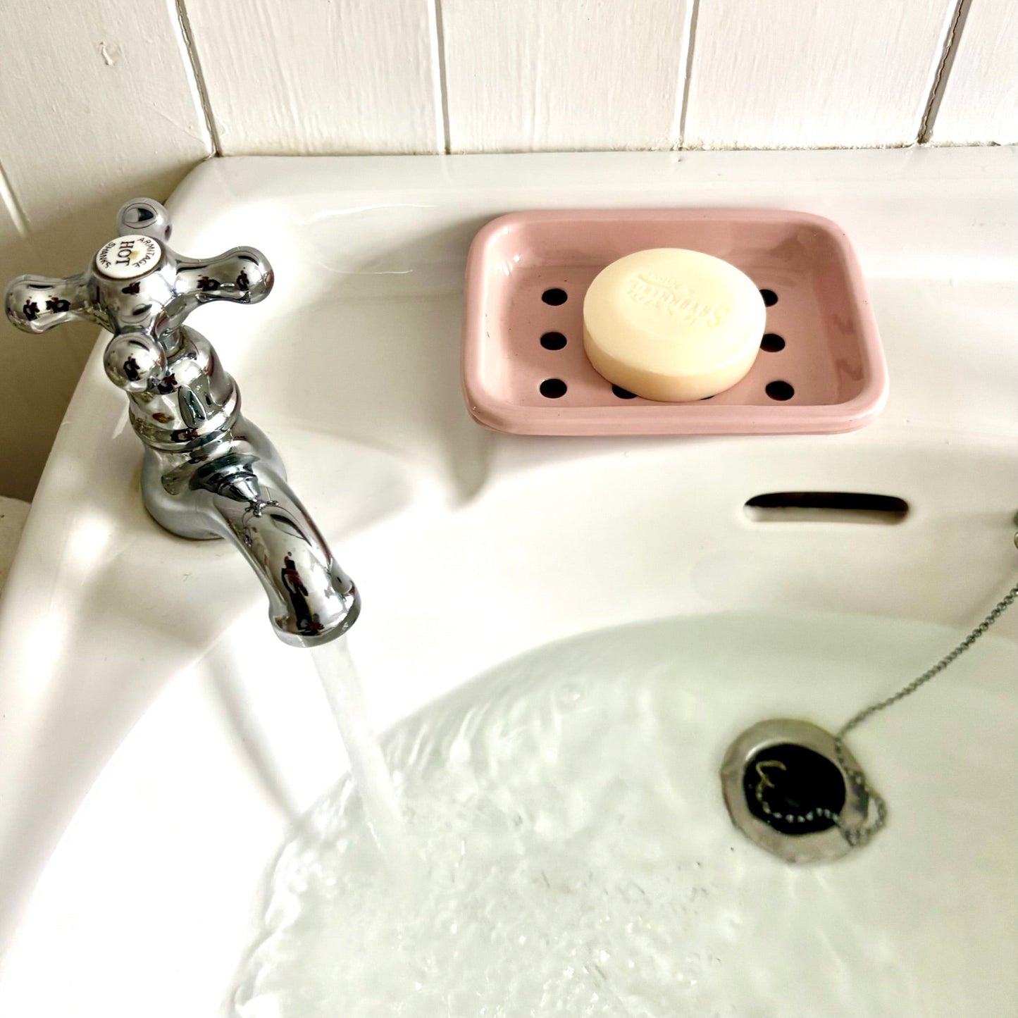 Pink soap dish with a bar of soap on a white sink with a silver faucet.