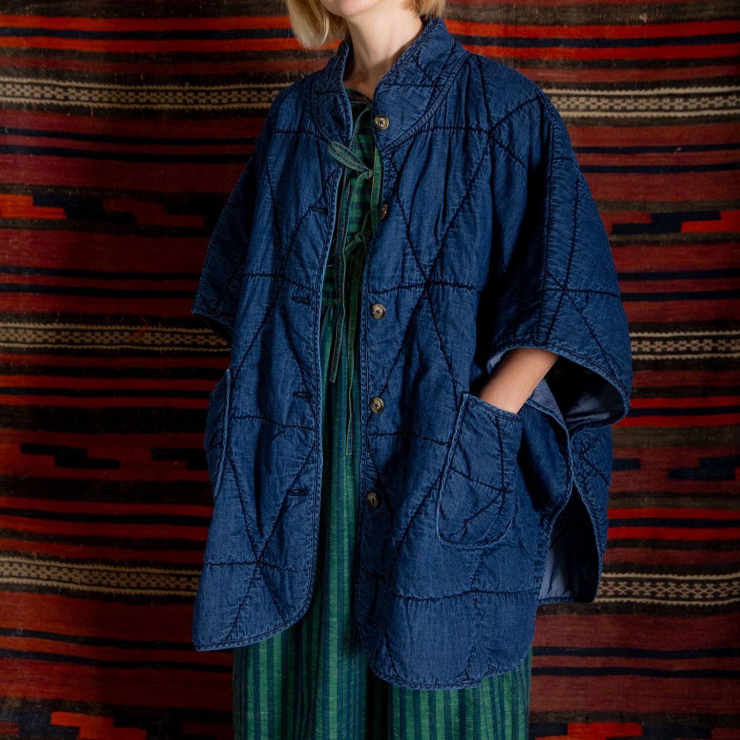 Person wearing a blue jacket over a green dress against a patterned red and black background