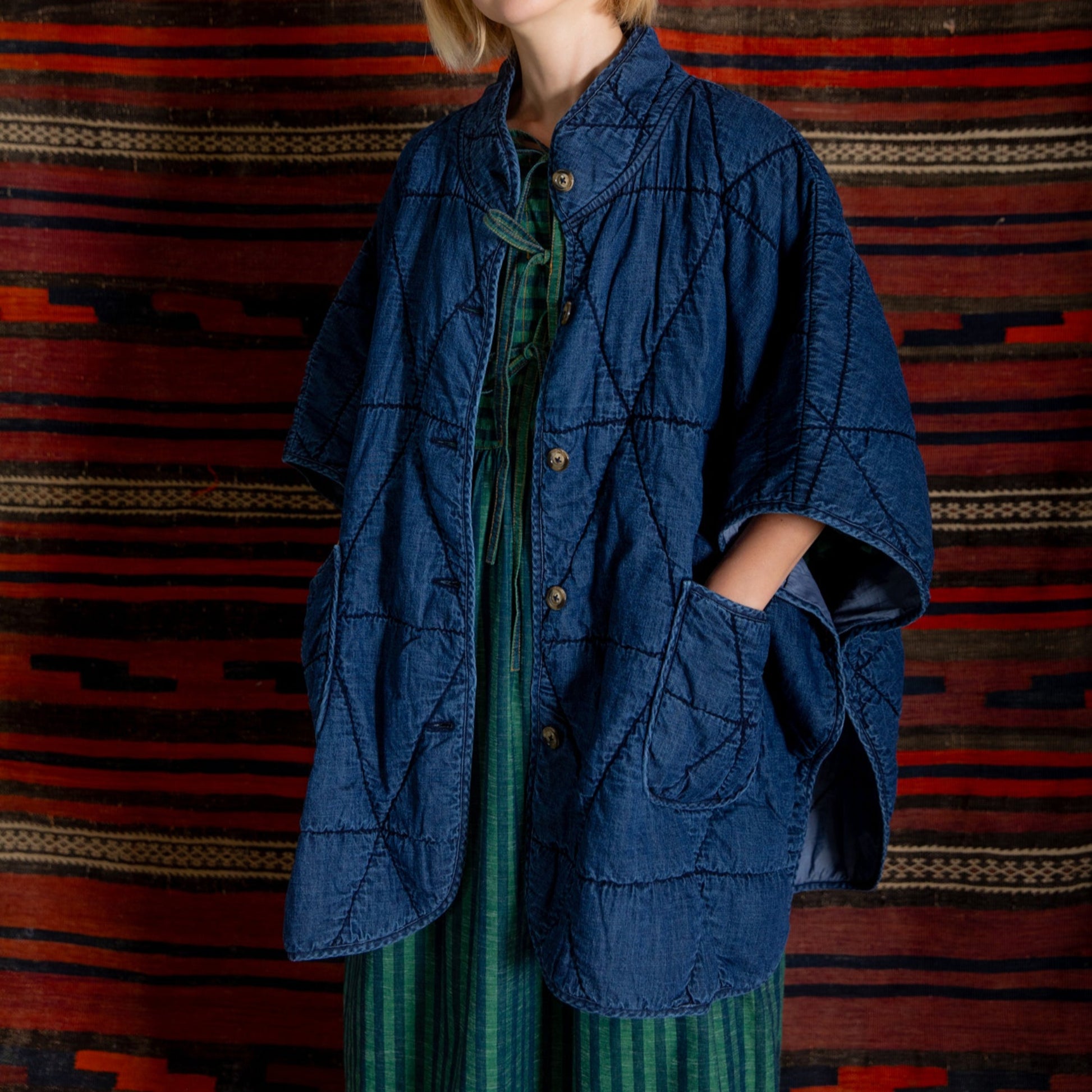 Person wearing a blue jacket over a green dress against a patterned red and black background