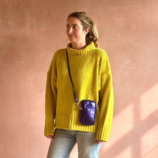 Woman wearing a yellow sweater with a purple crossbody bag against a pink wall
