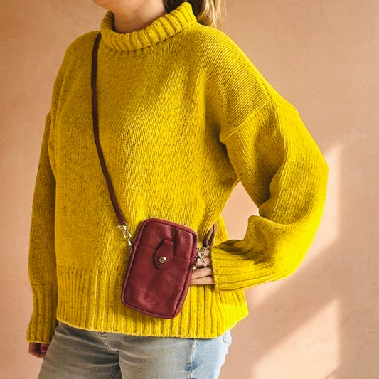 Person wearing a yellow sweater with a maroon crossbody bag on a beige background