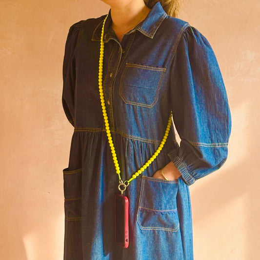 Person wearing a blue denim dress with a yellow lanyard and red phone case against a beige background