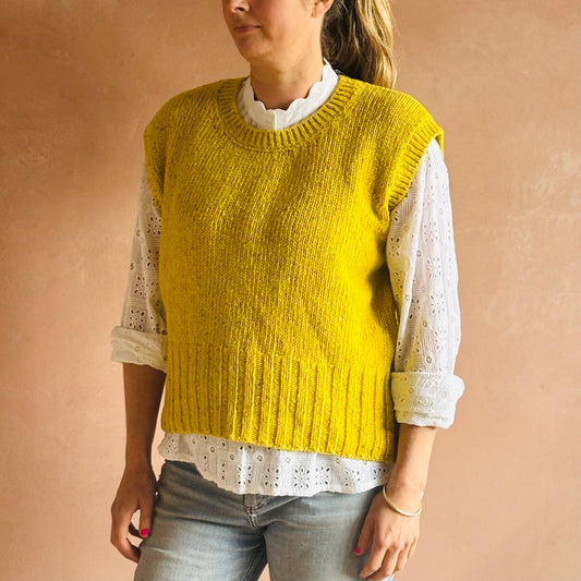 Person wearing an Irish yellow knitted vest over a white lace shirt on a beige background