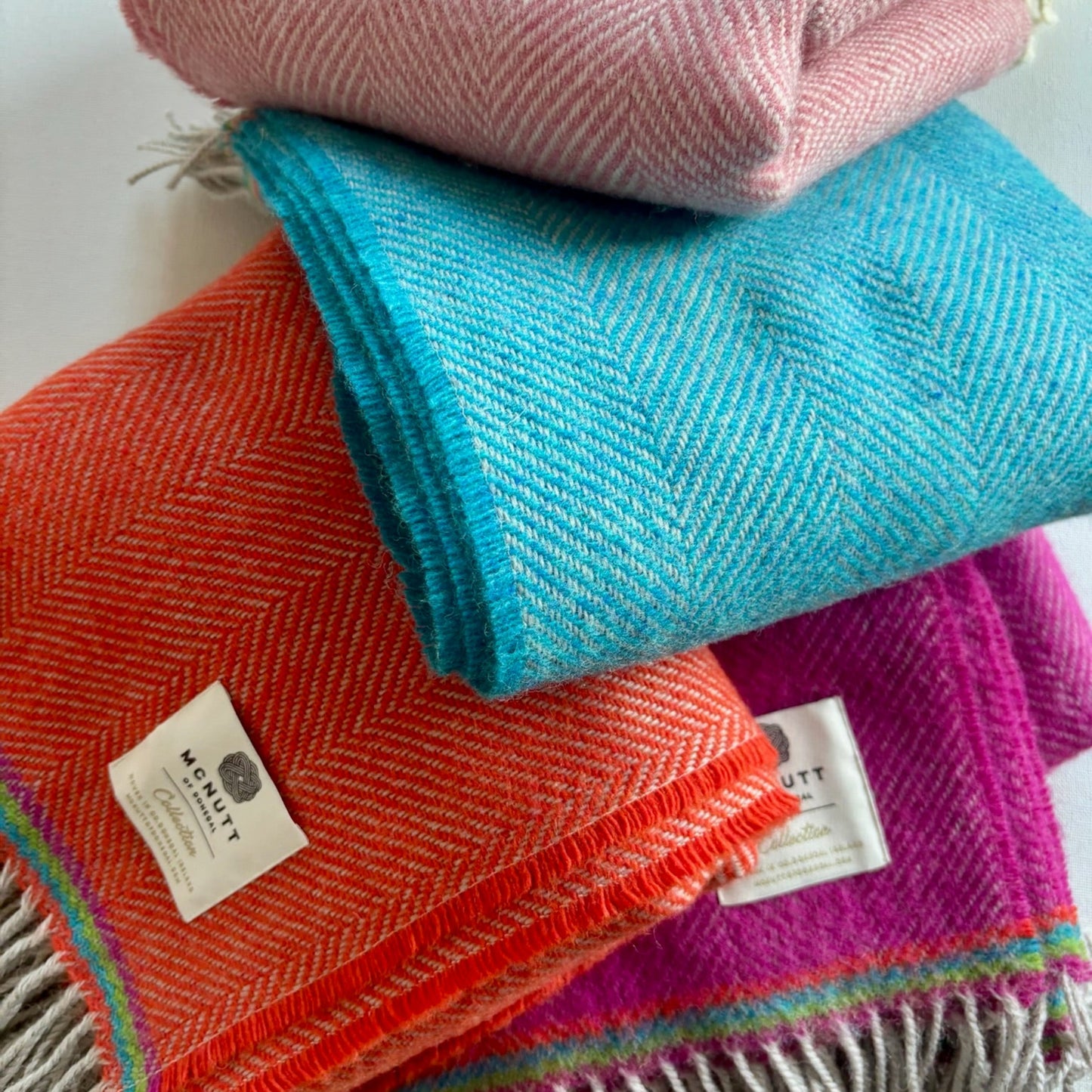 Stack of colorful woven blankets with visible brand labels on a white background