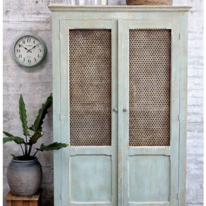 Vintage-style cabinet with wicker doors next to a clock and plant on a textured wall.