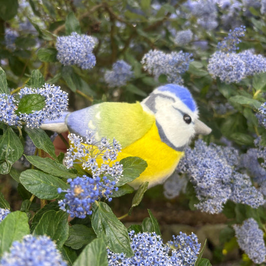 Toy bird among blue flowers and green leaves
