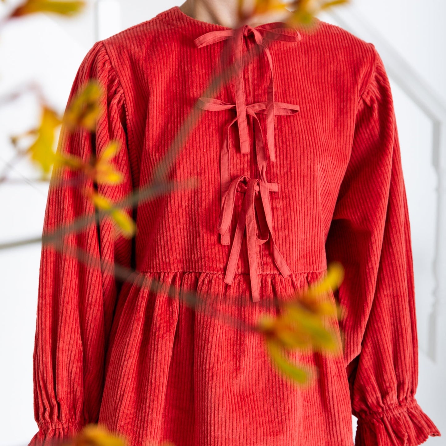 Red corduroy blouse with a white background and blurred autumn leaves.
