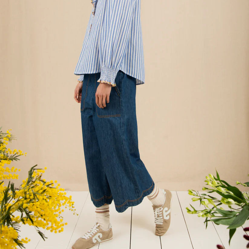 Woman wearing a blue striped shirt and jeans standing in a room with yellow flowers.