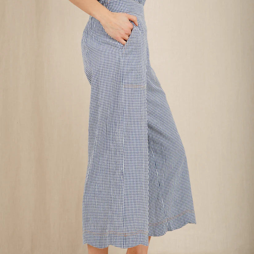 Person wearing a blue checkered dress with wide-leg pants on a beige background