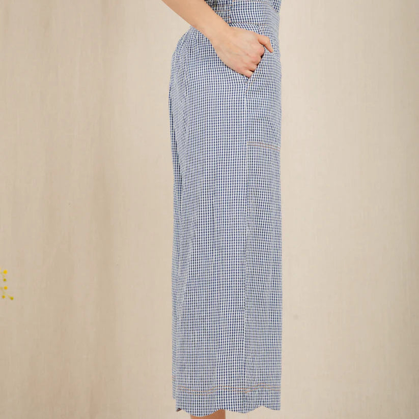 Person wearing a blue checkered dress with ruffled top on a beige background