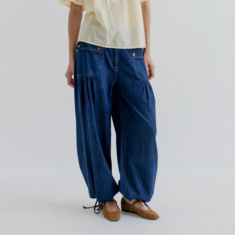 Woman wearing a light yellow blouse and blue wide-leg pants on a plain background