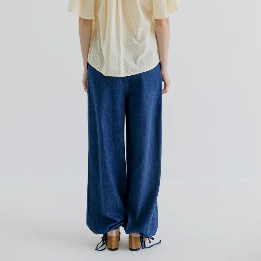 Person wearing a light-colored top and blue pants on a plain background