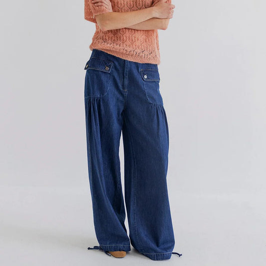 Woman wearing a pink sweater and blue pants on a plain background