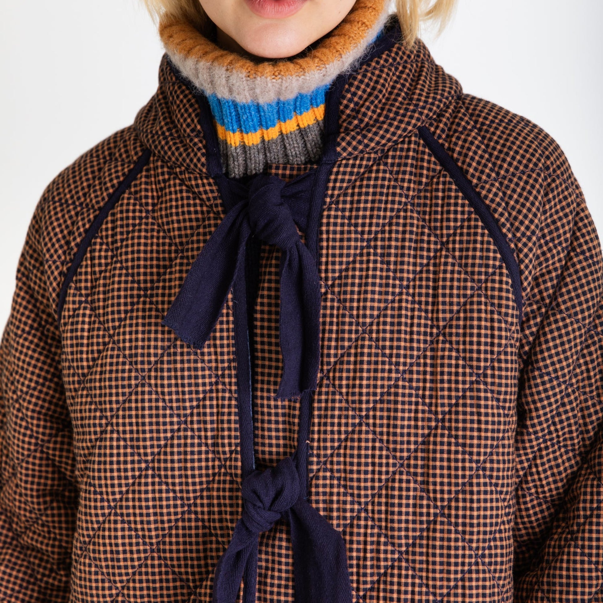 Person wearing a brown checkered coat with a blue tie and multicolored turtleneck.