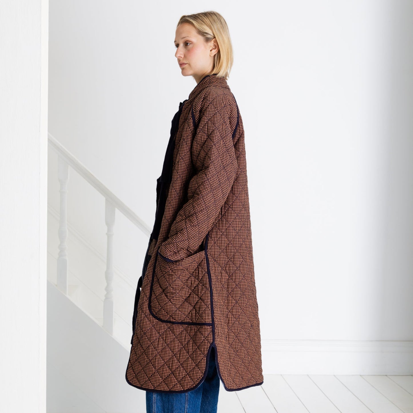 Person wearing a brown quilted coat in a minimal white room