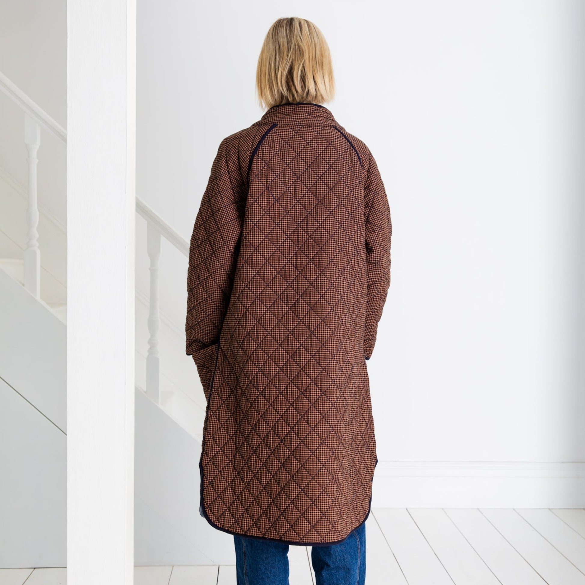 Person wearing a long quilted brown coat in a white room