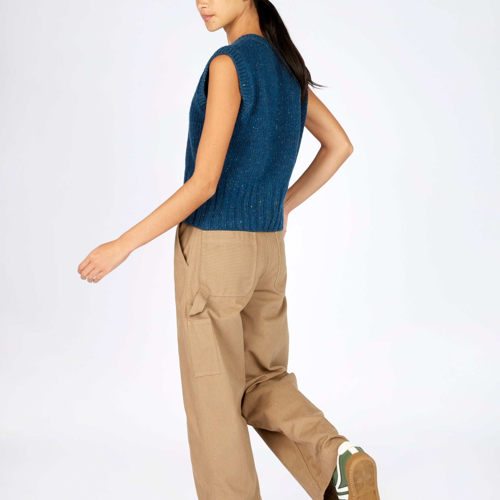 Woman wearing a blue sleeveless sweater and beige pants on a white background