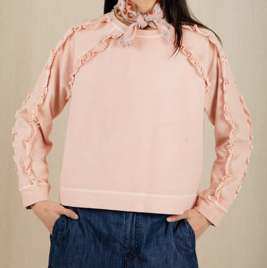 Woman wearing a pink blouse with ruffled sleeves against a beige background