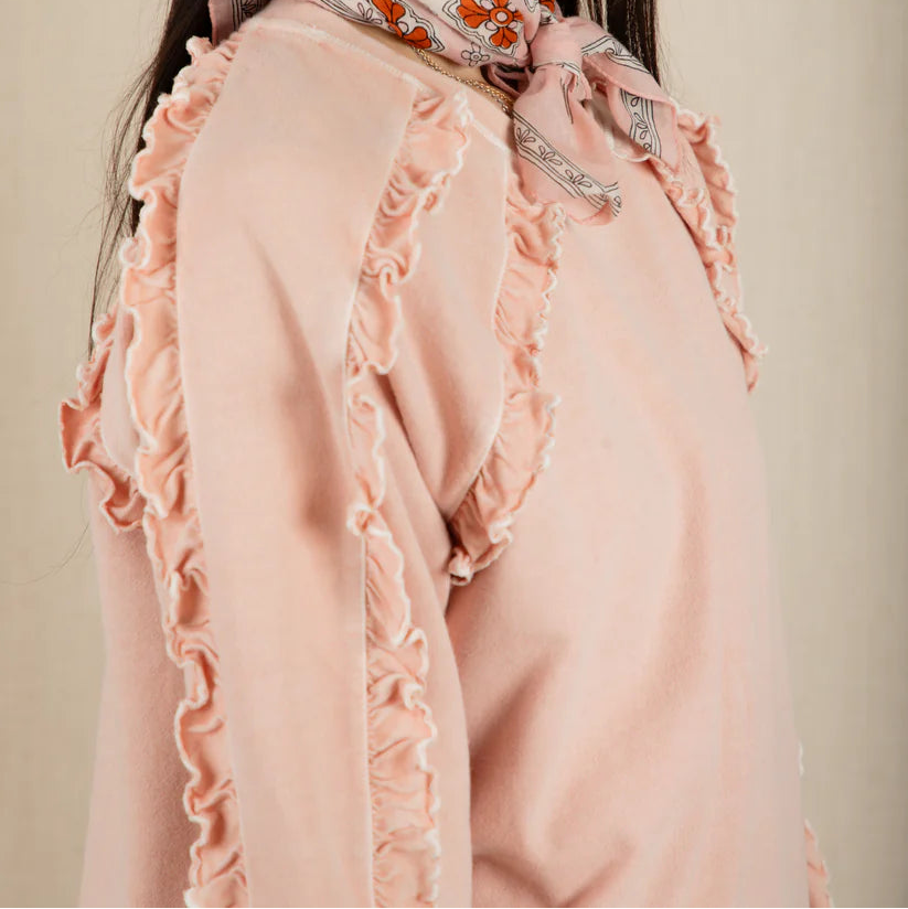 Woman wearing a pink blouse with ruffled details and a patterned scarf on a beige background