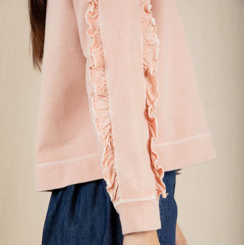 Person wearing a pink blouse with ruffled sleeves and blue pants on a beige background