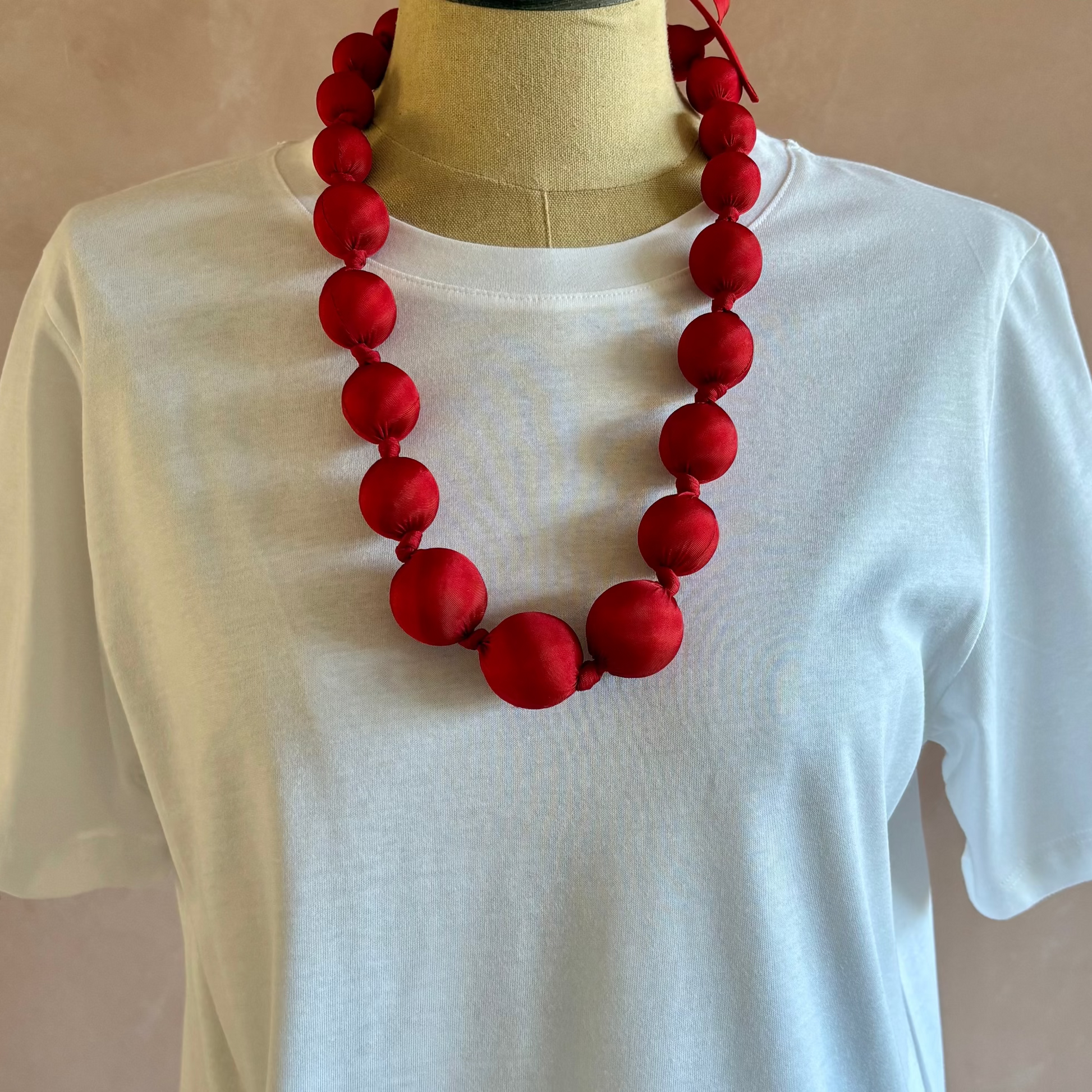 Red necklace on a mannequin wearing a white shirt against a beige background