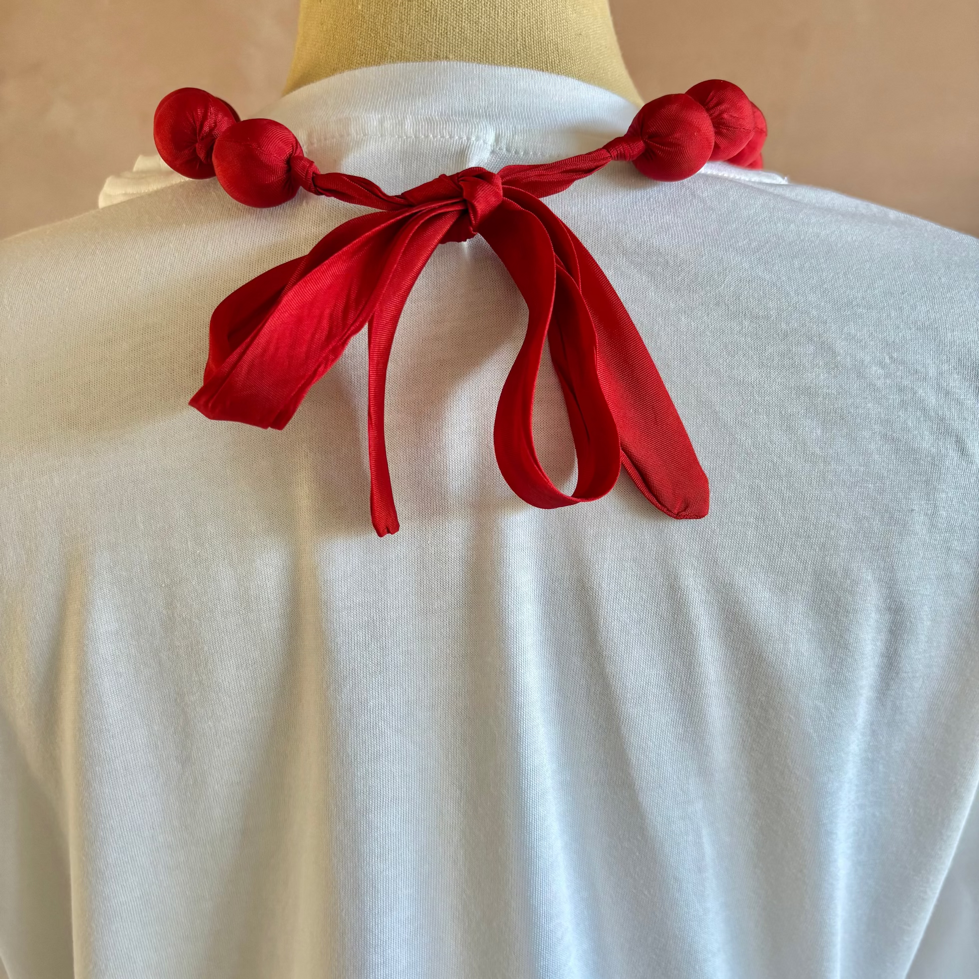 White garment with red decorative elements on a mannequin against a beige background
