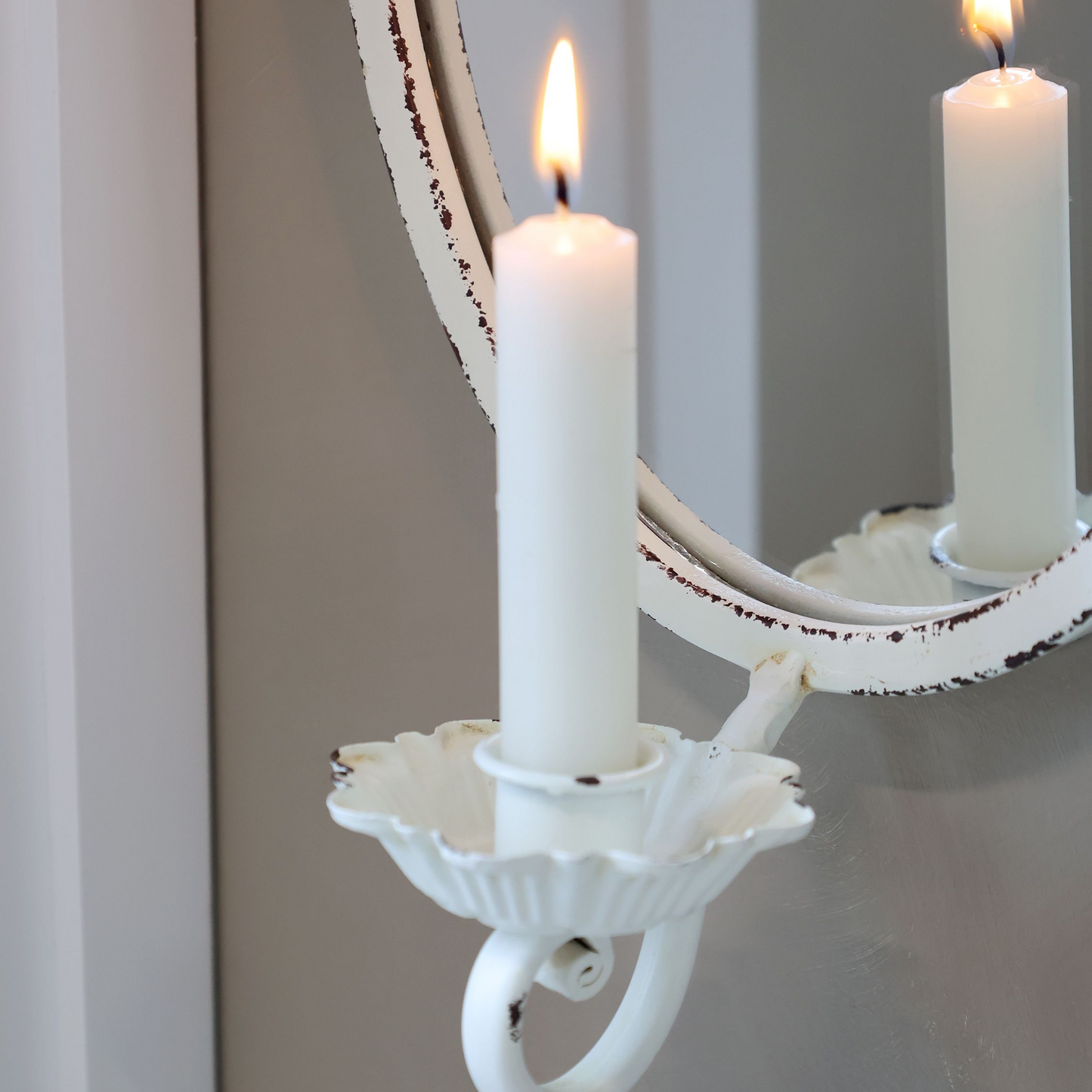 Decorative wall sconce with two lit candles in front of a mirror on a gray wall.